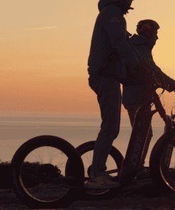 Deux personnes en trottinette électrique au coucher du soleil.