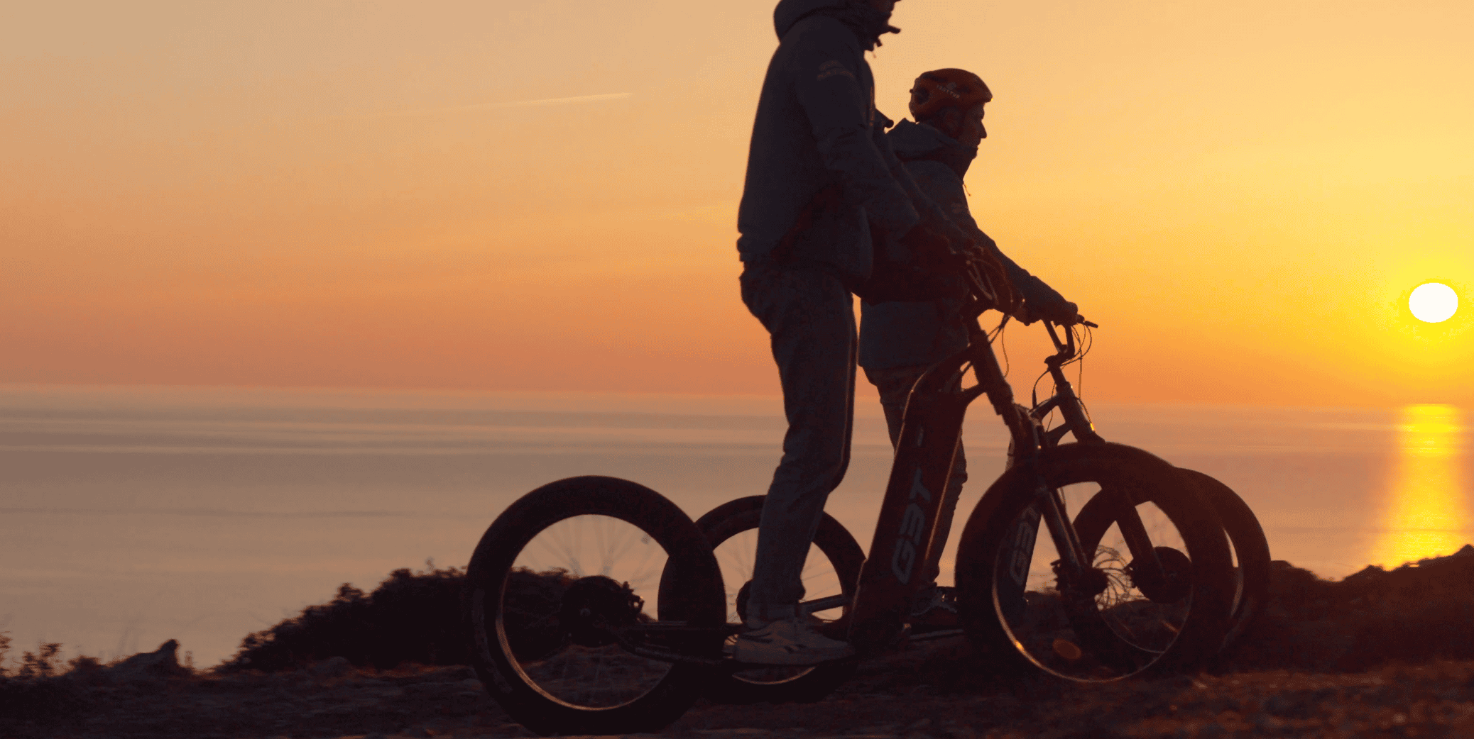 Deux personnes en trottinette électrique au coucher du soleil.